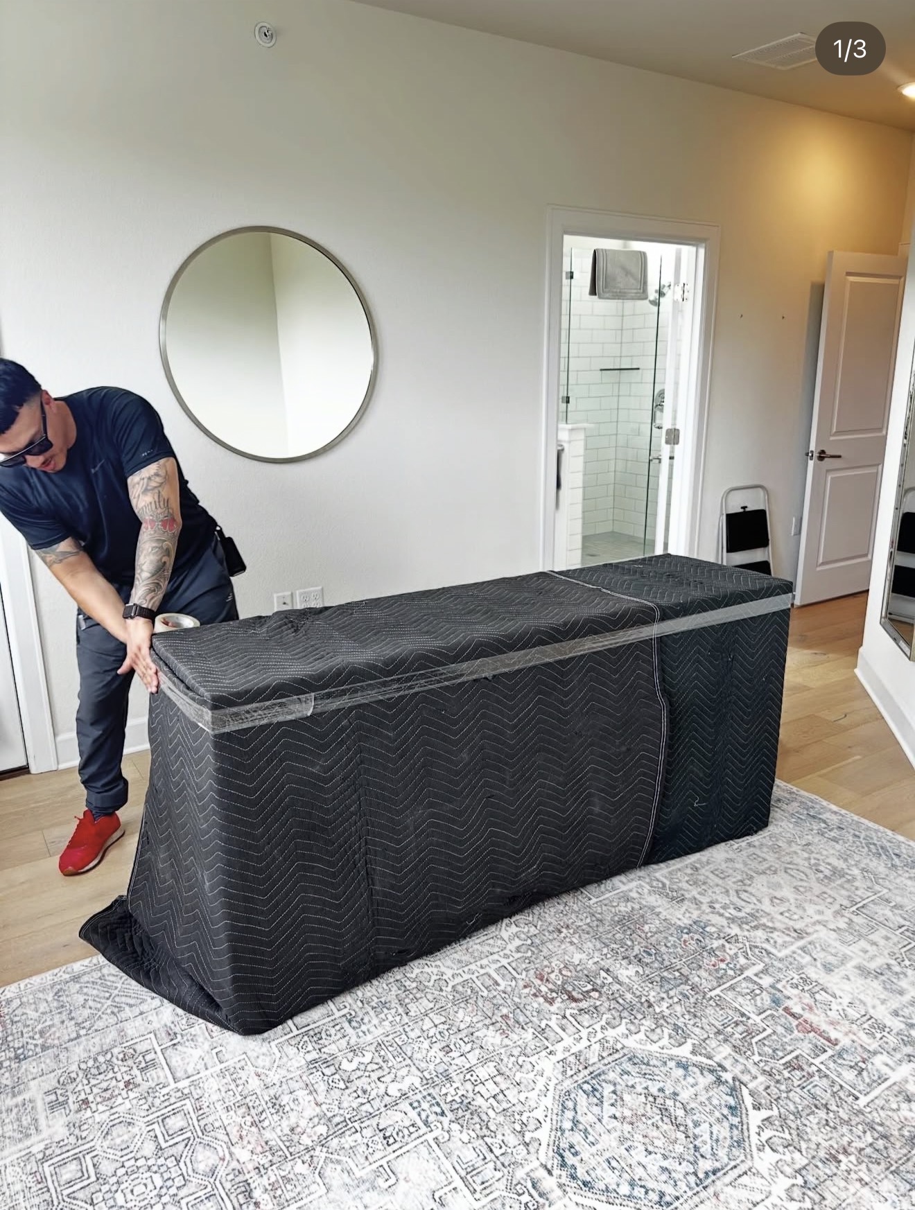 Lovable Movers crew member securing a moving blanket around a long console with stretch wrap in a bedroom