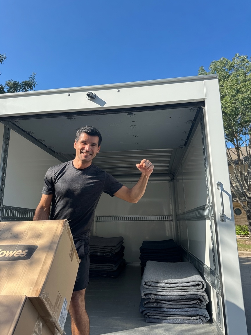 Smiling Lovable Movers crew member flexing while carrying a box out of a loaded moving truck in Austin, Texas