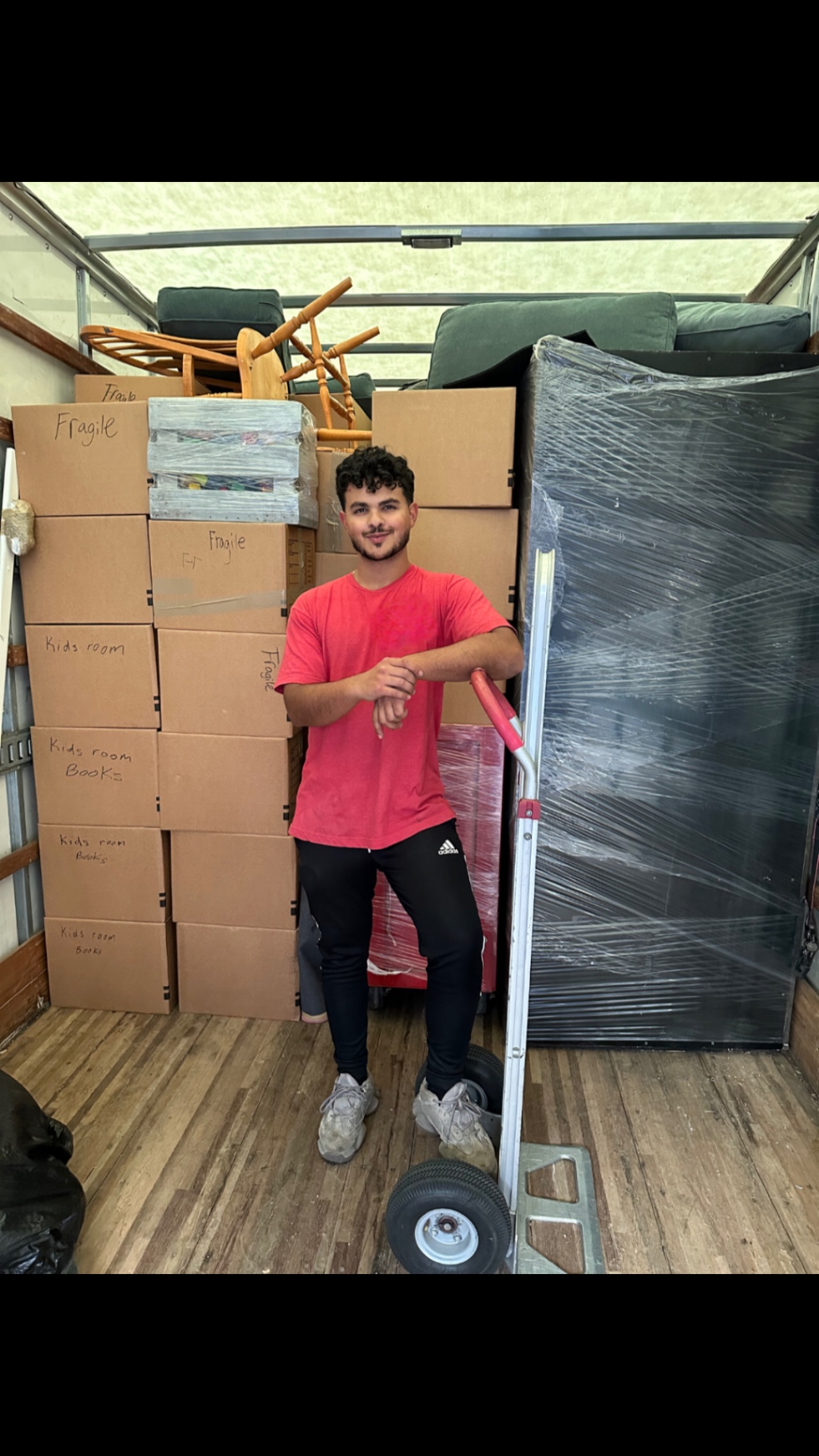 Lovable Movers crew member standing beside a fully loaded truck packed with labeled boxes and a wrapped mattress