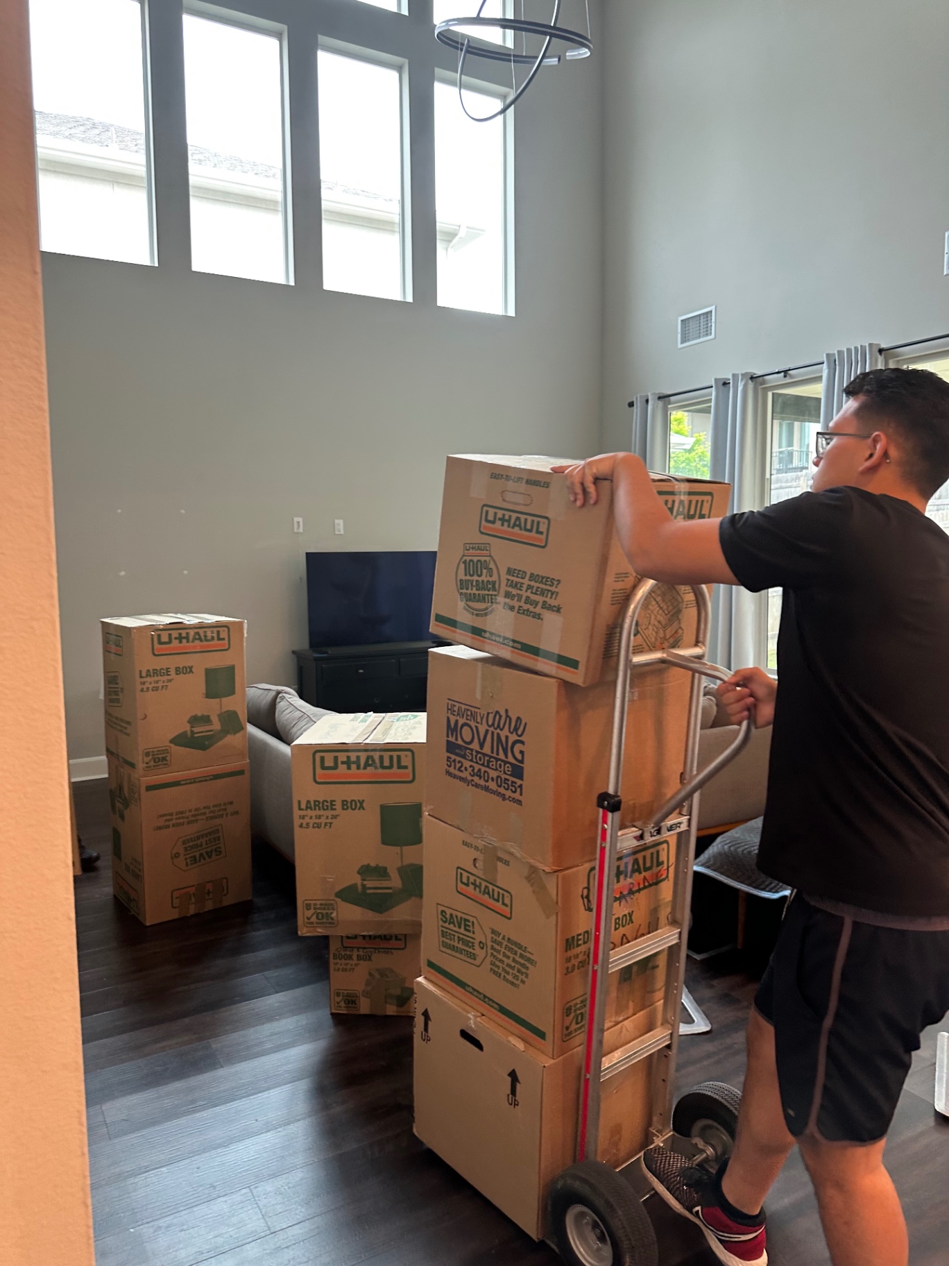 Mover using a hand truck to stack U-Haul boxes in a bright Austin living room