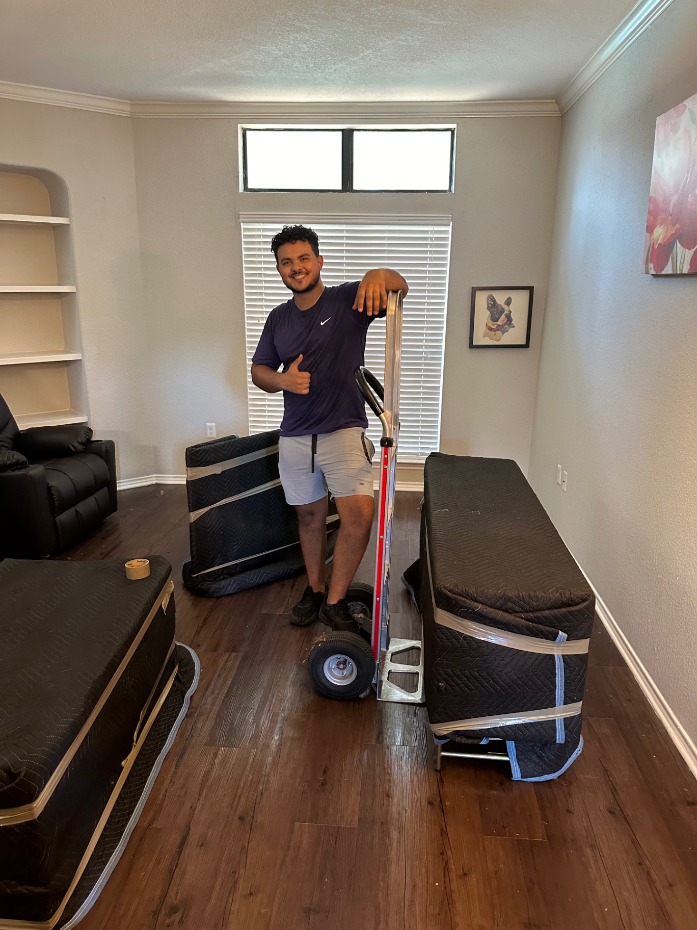 Lovable Movers crew member with a hand truck beside mattresses padded and wrapped for a move